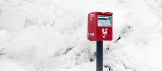 Świąteczne kartki pocztowe leżące na śniegu obok skrzynki na listy