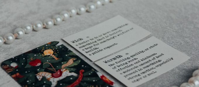 Stos kolorowych kartek świątecznych leżących na drewnianym stole obok gałązki choinki
